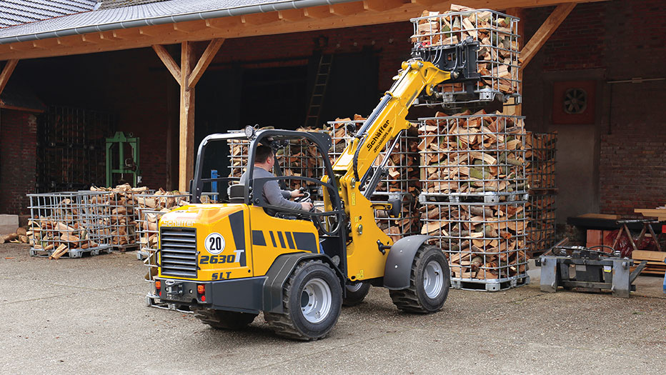 Schäffer 2630 T SLT carrying a cage with logs on a fork